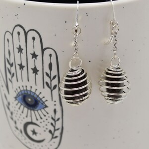 May include: A pair of silver dangle earrings with black gemstone caged in a silver wire spiral.