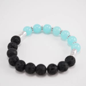 Pode incluir: Um bracelete feito com contas de rocha vulcânica preta e contas de pedras preciosas azuis claras.