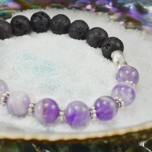 May include: A purple amethyst and black lava rock beaded bracelet with silver spacers. The bracelet is on a white background.