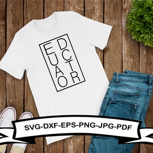 May include: White t-shirt with black text that reads "EDUCATOR" in a vertical block design. The shirt is on a wooden surface with a pair of jeans and a plant in the background.