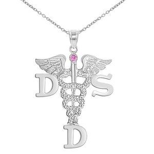 May include: Silver necklace with a medical caduceus pendant featuring the letters D, S, and D. The pendant has a pink gemstone at the top.