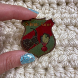 May include: A red, green, and black shield-shaped sticker with the text "Schrute Farms" and a goat and beet design.