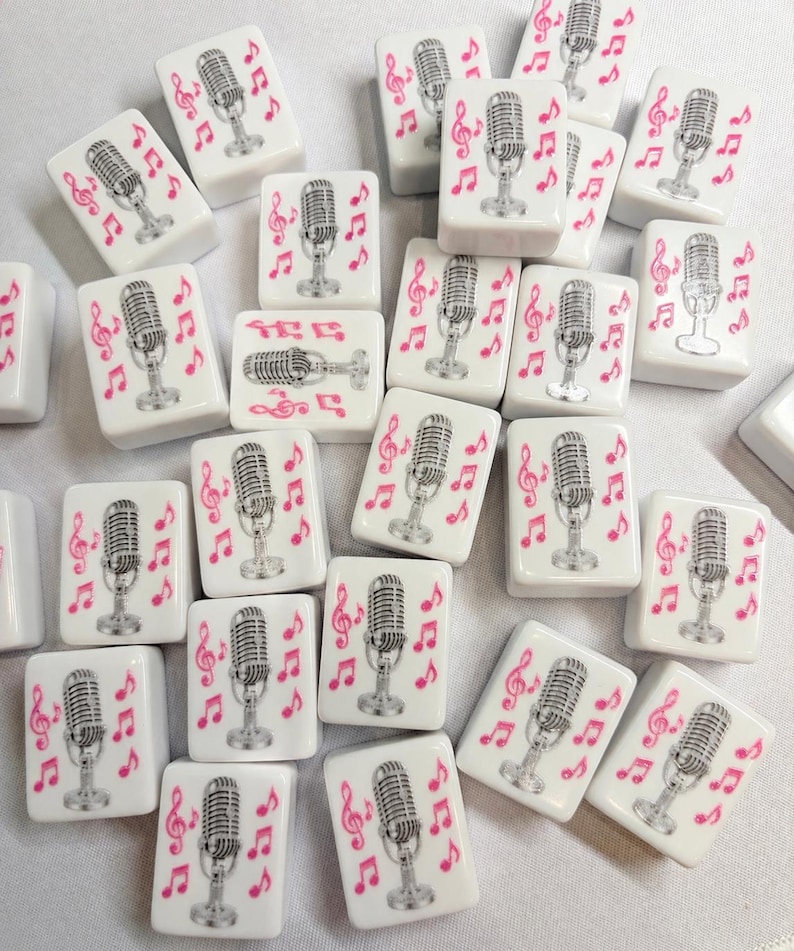 May include: A collection of rectangular white tiles, each featuring a silver vintage-style microphone graphic surrounded by small pink musical notes. The tiles are scattered across the frame, displaying a consistent design on each individual piece.