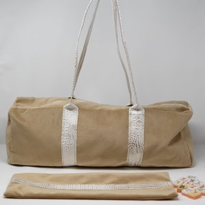 May include: A beige velvet travel bag with white crocodile embossed leather trim and two top handles. The bag is lying flat on a white surface with a matching beige velvet pouch and a set of dominoes.