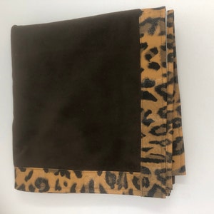 May include: A brown throw blanket with a leopard print border. The blanket is folded and the border is visible on all sides.