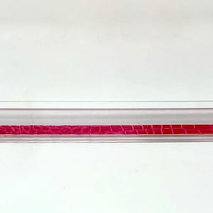 Könnte beinhalten: Ein klares Plastikregal mit einem rosa Krokodilprägemuster am Boden.