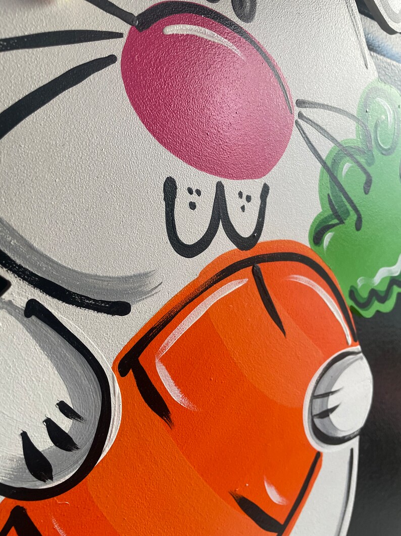 May include: A white bunny with a pink nose and black eyes is holding a carrot in its paws. The bunny is painted on a black background with green and orange accents.