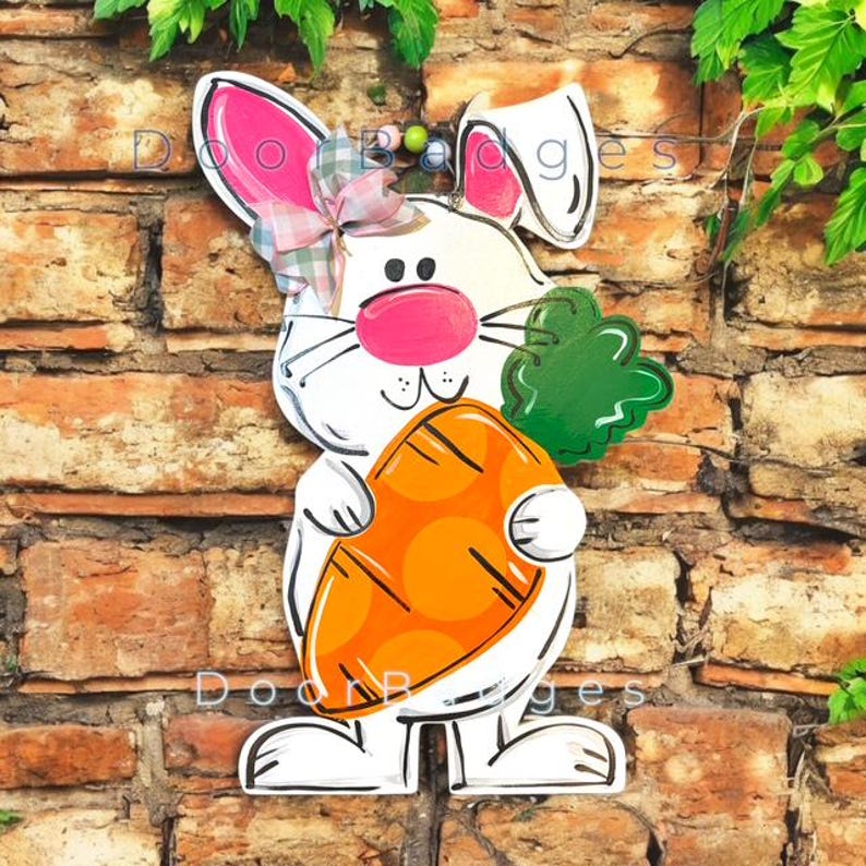 May include: White bunny rabbit holding a carrot with green leaves. The bunny has pink ears, a pink nose, and a pink bow. The carrot is orange with brown spots.