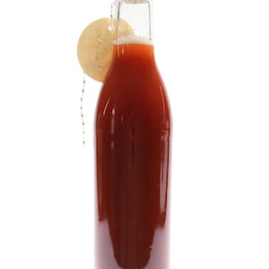 May include: A glass bottle with a black lid filled with a red liquid. A brown tag with the word "Merci" is tied around the neck of the bottle.