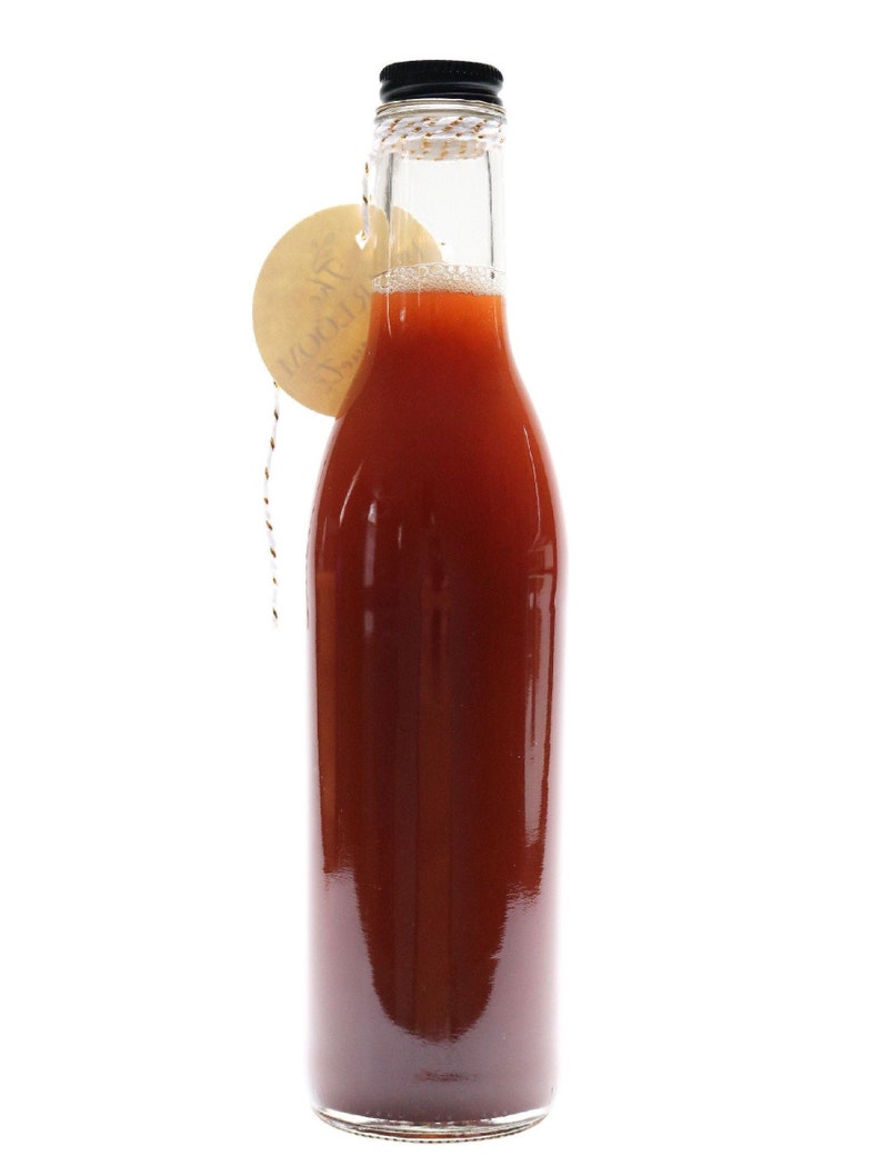 May include: A glass bottle with a black lid filled with a red liquid. A brown tag with the word "Merci" is tied around the neck of the bottle.