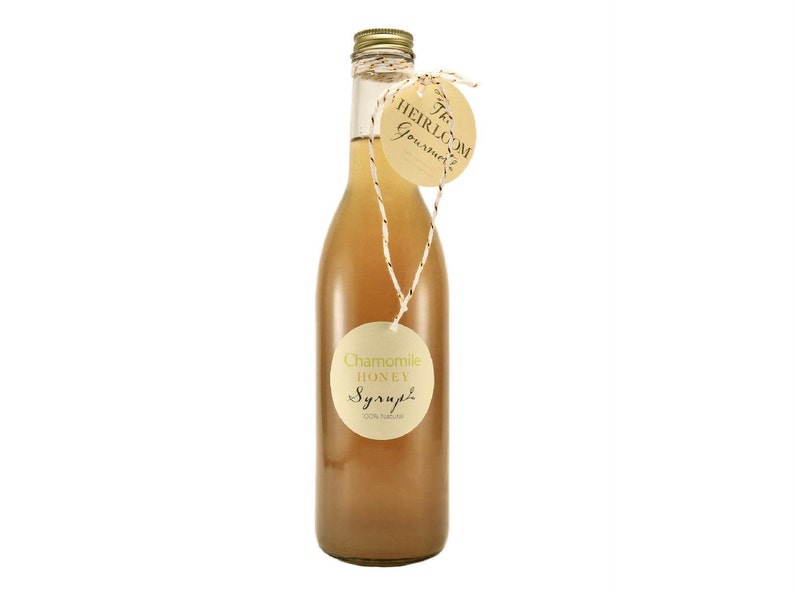 Puede incluir: Una botella de vidrio de jarabe de miel de manzanilla con una etiqueta marr&oacute;n que dice "Jarabe de miel de manzanilla 100% natural". La botella est&aacute; atada con un cordel y una etiqueta redonda que dice "The Heirloom Gourmet".