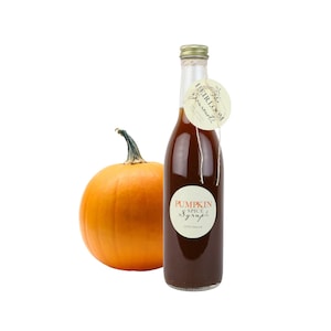 May include: A glass bottle of pumpkin spice syrup with a brown label that says "Pumpkin Spice Syrup 100% Natural" and a tag that says "Heirloom Gourmet". A small orange pumpkin is next to the bottle.