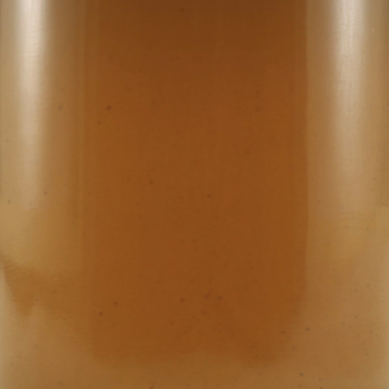 Puede incluir: Primer plano de una botella de vidrio transparente llena de un l&iacute;quido marr&oacute;n claro. El l&iacute;quido tiene peque&ntilde;as part&iacute;culas suspendidas en &eacute;l.