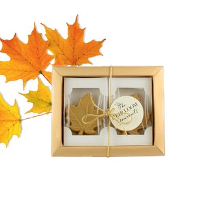 May include: A gold gift box with two maple leaf shaped candies inside. The box is tied with a brown ribbon and has a small tag that says "The Heirloom Gourmet".