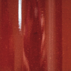 May include: A close-up of a glass jar filled with a thick, red liquid. The liquid has a slightly textured surface and appears to be a sauce or condiment.