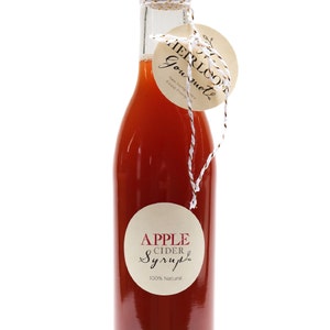 May include: A glass bottle of apple cider syrup with a brown label that says "APPLE CIDER Syrup 100% Natural". The bottle is tied with twine and a brown tag that says "HERLOOM Gourmet New Hampshire's Finest Products".