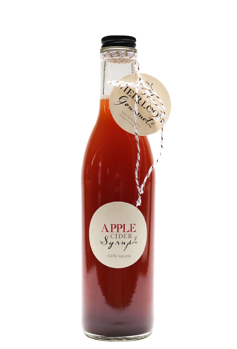 May include: A glass bottle of apple cider syrup with a brown label that says "APPLE CIDER Syrup 100% Natural". The bottle is tied with twine and a brown tag that says "HERLOOM Gourmet New Hampshire's Finest Products".