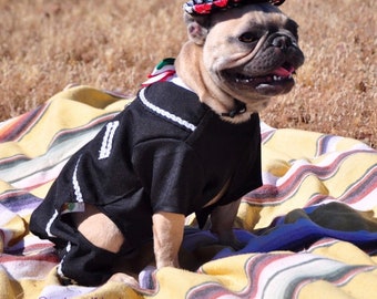 May include: A French Bulldog wearing a black mariachi outfit with white trim and a matching sombrero. The dog is sitting on a striped blanket outdoors. The image includes the text "@nachoandfriends".