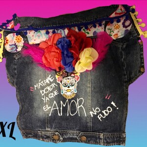 May include: A blue denim jacket with a floral trim and a skull with flowers design. The jacket has the text "M&aacute;t&aacute;me Dolor Ya Que El Amor No Pudo!" embroidered on the front.