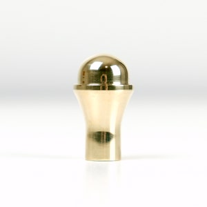 May include: A gold-toned bottle stopper with a rounded top and a flared base.