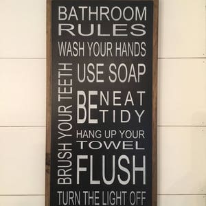 May include: Black framed sign with white text that reads "Bathroom Rules" and lists rules for bathroom etiquette, including "Wash your hands", "Use soap", "Brush your teeth", "Be tidy", "Hang up your towel", "Flush", and "Turn the light off".