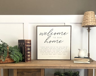 May include: A wooden sign with the text "Welcome to our home" in black script font. Below the text is a bible verse: "Those who live in the shelter of the Most High will find rest in the shadow of the Almighty. This I declare about the Lord: He alone is my refuge, my place of safety; He is my God, and I trust him. Psalm 91:1-2"