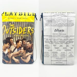 Könnte beinhalten: Eine Clutch-Tasche mit Reißverschluss, bedruckt mit dem Programmheft-Design für "The Outsiders: A New Musical". Die Vorderseite zeigt ein Foto der Besetzung, die Rückseite die Liste. Der obere Teil ist gelb und trägt die Aufschrift "PLAYBILL" und "Bernard B. Jacobs Theatre".