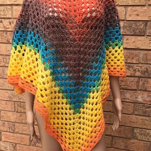 May include: A colorful crochet poncho with a rainbow ombre pattern. The poncho is made with a loose, open stitch and has a triangular shape.