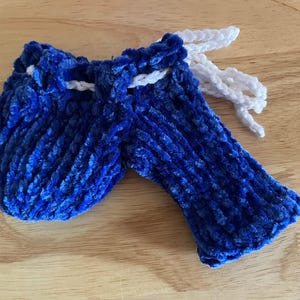 Puede incluir: Una bolsa de terciopelo azul hecha a mano con cierre de cordón y una manga a juego. La bolsa y la manga están hechas de un material suave y texturizado. El cordón es blanco.