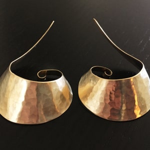 May include: A pair of gold-toned hammered metal earrings with a curved, open design and a spiral detail at the top.