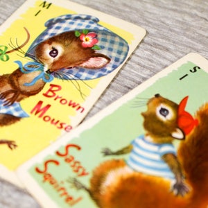 May include: Three illustrated cards from a children's game. The cards feature a brown mouse wearing a blue and white gingham dress and hat, a squirrel wearing a red and white striped shirt and a red hat, and a fox wearing a red and white striped shirt. The cards are labeled "Brown Mouse", "Sassy Squirrel", and "Foxy Fox".
