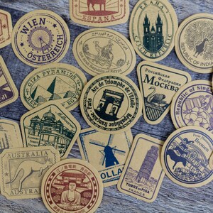 May include: A collection of vintage-style travel-themed stickers. Each sticker features a different landmark or location, including the Eiffel Tower, Mount Fuji, and the Leaning Tower of Pisa. The stickers are in shades of brown, green, and purple.