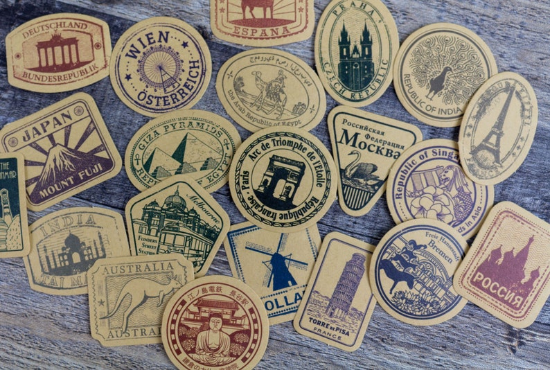 May include: A collection of vintage-style travel-themed stickers. Each sticker features a different landmark or location, including the Eiffel Tower, Mount Fuji, and the Leaning Tower of Pisa. The stickers are in shades of brown, green, and purple.