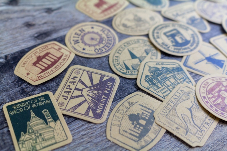 May include: A collection of vintage-style travel stickers with various designs and text. The stickers feature illustrations of landmarks and country names, including Japan, Australia, and Germany. The color palette includes shades of brown, blue, and purple.