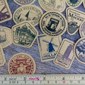 May include: A collection of vintage-style travel stickers featuring landmarks from around the world. Designs include Mount Fuji, the Eiffel Tower, and the Taj Mahal. A ruler shows measurements in inches.