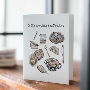 Może przedstawiać: Biała kartka z tekstem "to the world's best baker" w czarnym kolorze. Na kartce znajduje się akwarelowa ilustracja różnych akcesoriów do pieczenia, w tym bochenek chleba, miska, słoik, wałek i nóż.