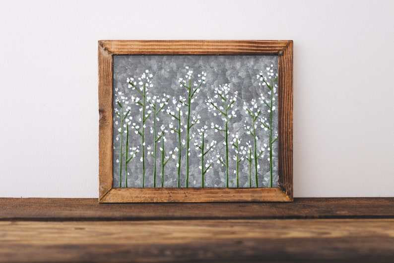 May include: A framed painting depicting a grey background with white flowers and green stems. The frame is made of wood and has a rustic appearance.