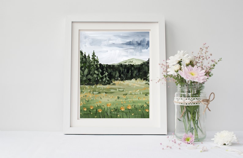 May include: A framed painting of a landscape with a forest in the background and a field of yellow flowers in the foreground. The sky is cloudy and gray.