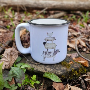 May include: White ceramic mug with a black rim. The mug features a watercolor illustration of a cow, sheep, pig, and chicken stacked on top of each other.