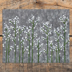 May include: A grey metal wall art piece with a white floral design. The flowers are painted in a simple, minimalist style.