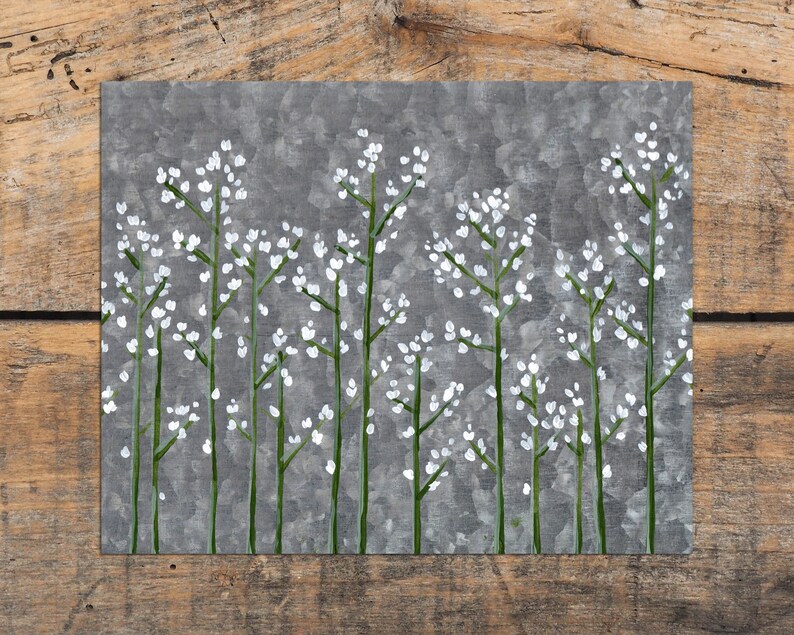 May include: A grey metal wall art piece with a white floral design. The flowers are painted in a simple, minimalist style.