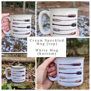 May include: Two ceramic mugs with a design of five brown wooden paddles on a white background. The top mug is cream colored with speckles and the bottom mug is white. The text "Cream Speckled Mug (top)" and "White Mug (bottom)" is printed below the mugs.