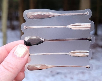 May include: A clear sticker sheet with a design of four wooden paddles, each with a different wood grain pattern. The paddles are arranged vertically, with the top paddle being the largest and the bottom paddle being the smallest.