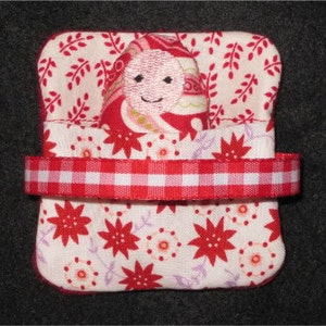 May include: A small, handmade doll with a pink face and a red and white patterned dress is tucked into a red and white fabric pouch with a red and white gingham ribbon.