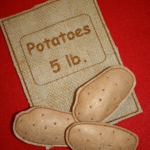 May include: A brown paper bag with the text "Potatoes 5 lb." printed on it. Three brown felt potatoes are in front of the bag.