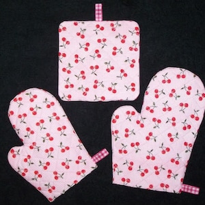 Puede incluir: Un juego de cocina acolchado rosa con un estampado de cerezas. El conjunto incluye dos guantes de horno y un salvamanteles cuadrado. Cada pieza tiene un pequeño lazo para colgar y un patrón de costura de diamante.
