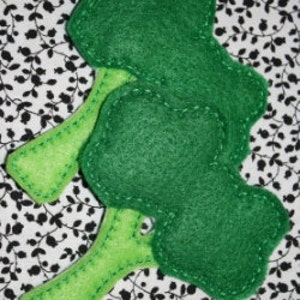 May include: Three green felt broccoli florets with green felt stems, sewn together. The florets are slightly rounded and have a textured surface. The stems are long and narrow.