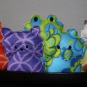 May include: Five plush toys in the shape of cats. The toys are made of soft fabric and have different patterns and colors. The toys are arranged in a row on a black surface.