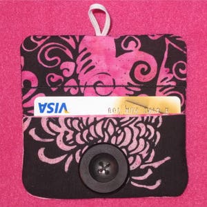 May include: Black fabric wallet with a pink floral design and a black button. The wallet has a slot for a credit card, which is visible in the image. The credit card has the VISA logo and the text "new haven auto x".