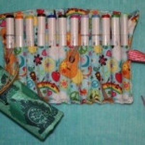 May include: A colorful fabric roll with a floral pattern and a pink and white ribbon. The roll is filled with 12 colorful markers.
